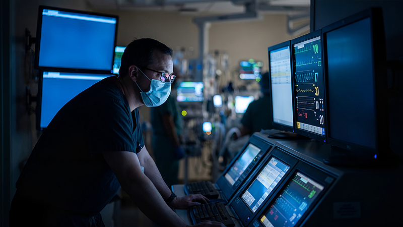 Medizinisches Fachpersonal, das in einem dunklen Kontrollraum die Vitalwerte eines Patienten überwacht. | Foto: ©Yasir – stock.adobe.com